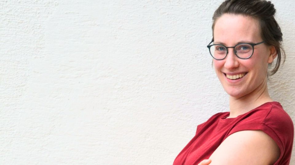 Seraphina Stöger steht lächelnd vor einer weißen Wand, Feldenkrais mit Seraphina Stöger in 1090 Wien